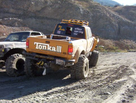 2000 Ford F-450 - Rear view of a yellow off-road pickup on a dirt trail, tailgate painted 'Tonka III' with 'Woodworks Unlimited' below it, 'atlas spring inc.…