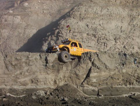2000 Ford F-450 - Distant shot of a yellow '84' off-road pickup perched on a narrow ledge partway up a steep quarry wall, front tire hanging over the edge as…