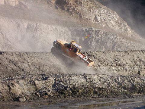 2000 Ford F-450 - Yellow off-road pickup pitched at a steep nose-up angle while charging up a dusty quarry hillclimb, kicking a cloud of dust off the loose b…