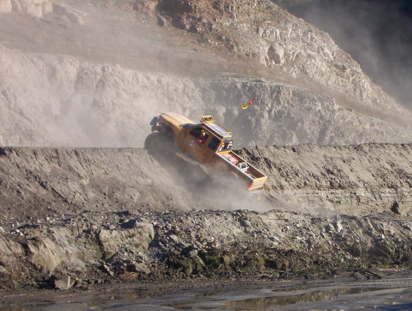 Yellow off-road pickup climbing a dusty quarry hill nose-up in dust