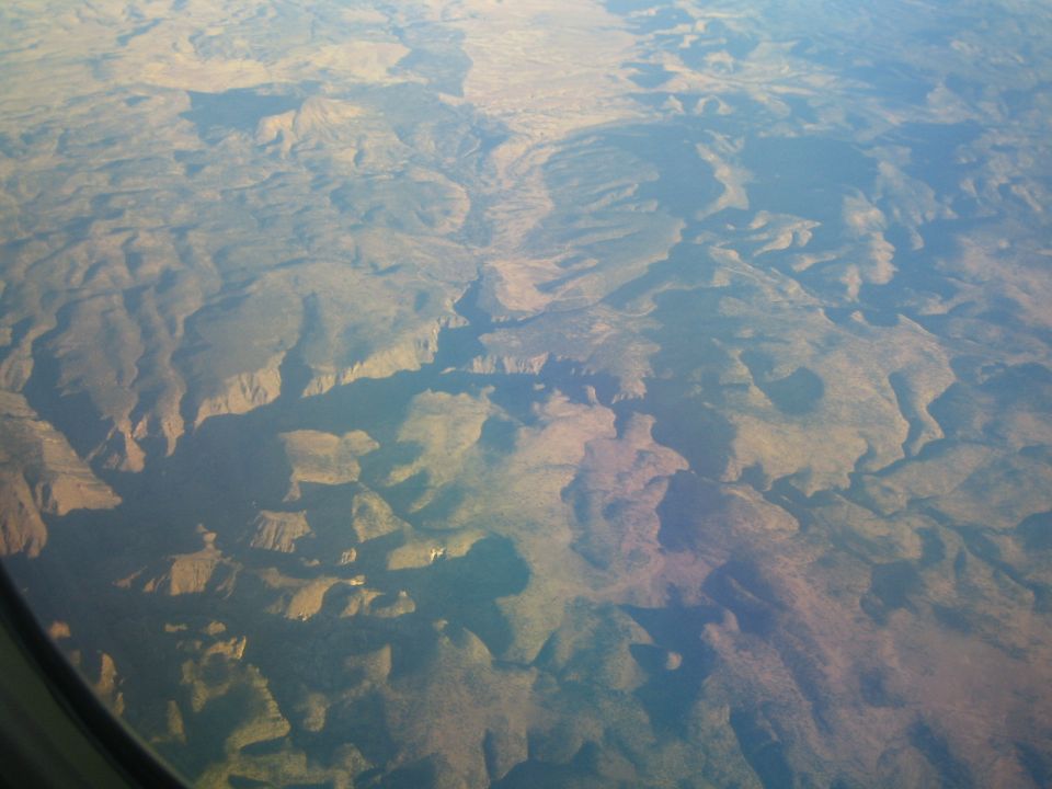 Aerial view of a vast canyon landscape with winding riverbeds and terrain under a hazy sky