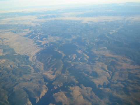 1968 Ford Mustang - An expansive aerial view captures the vastness of a desert landscape, characterized by canyons and mesas under a pale sky.