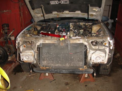 1992 Ford Taurus - Front end of a 1992 Ford Taurus SHO with the hood open and radiator exposed, indicating it is undergoing deconstruction.