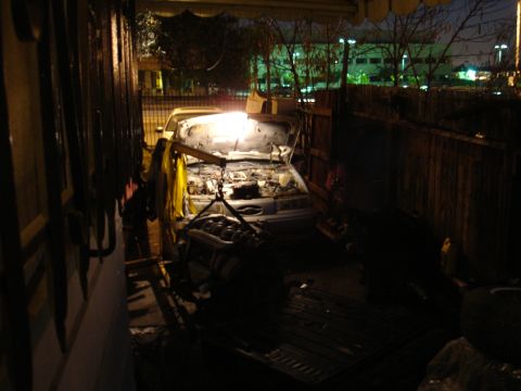 1992 Ford Taurus - Engine removal in progress at night, car hood is open and engine is suspended by a hoist.