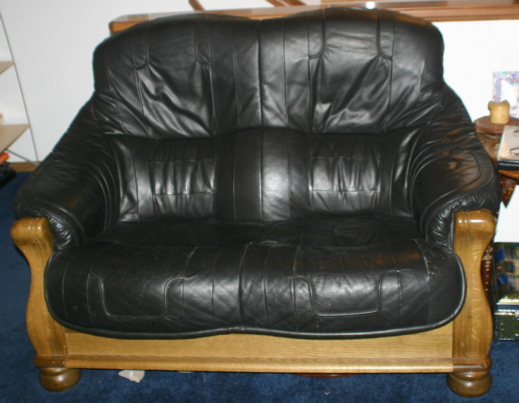 Black leather sofa with tufted cushions and carved wooden arms and base, viewed from the front