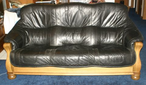 2003 Jeep TJ - Black leather sofa with wooden trim sits on a blue carpeted floor.