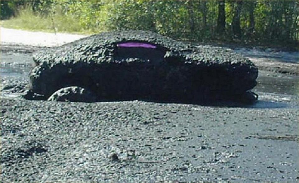 Vehicle completely covered in mud, stuck in a muddy area with trees in the background