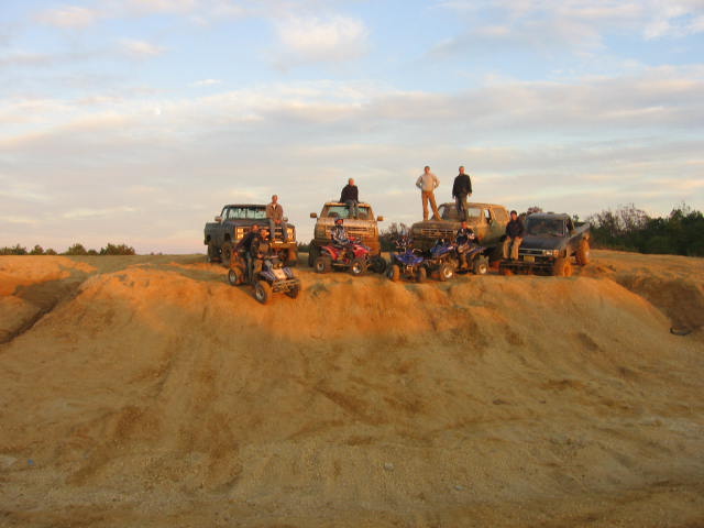 Several trucks and ATVs on a dirt hill with people standing around