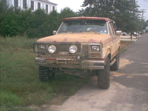 1986 Ford Bronco - This weathered Ford Bronco, likely from the early 1980s, sits parked on a dirt road.