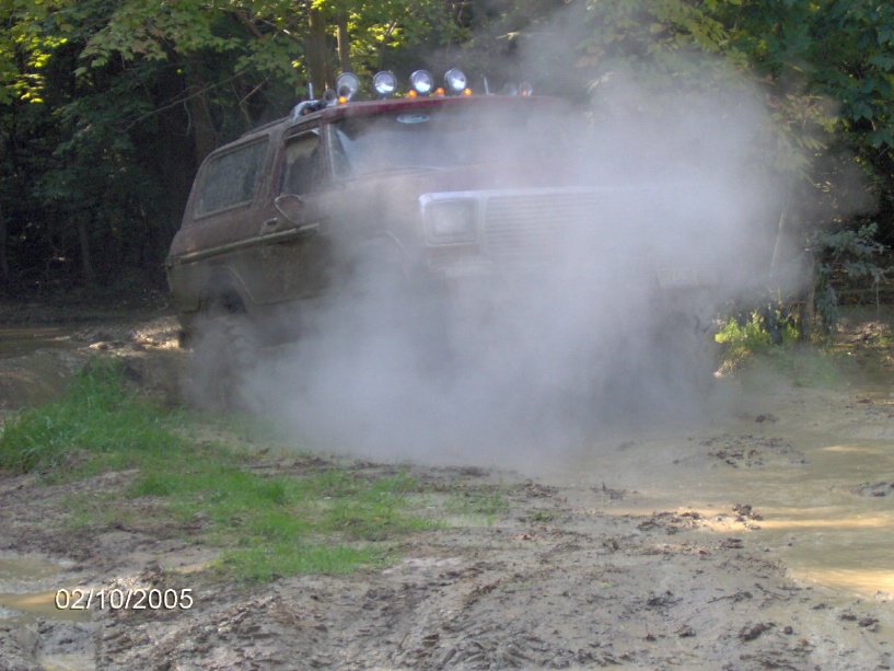 1978 Ford Bronco kicking up dust while driving through a muddy trail