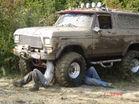 1978 Ford Bronco - Two mechanics work on a heavily modified 1978 Ford Bronco, covered in mud after off-roading.