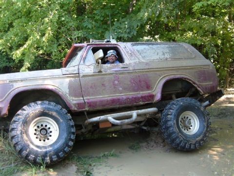 1978 Ford Bronco - A driver navigates a muddy off-road path in a heavily soiled 1978 Ford Bronco.