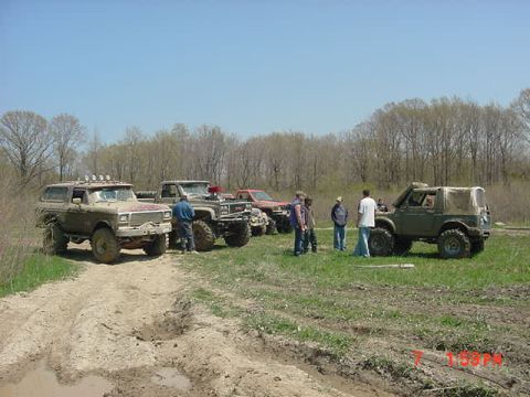 1978 Ford Bronco - Several off-road vehicles and a group of people gather in a grassy, wooded area on a sunny day.