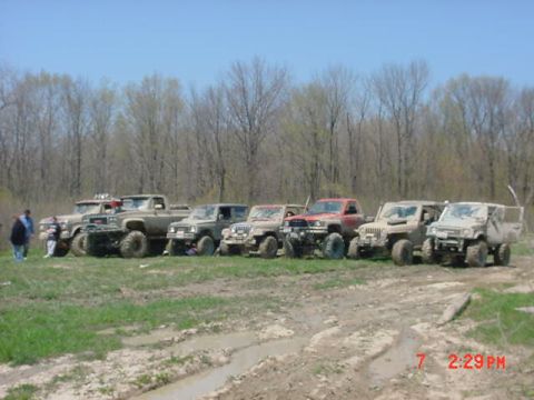 1978 Ford Bronco - A group of off-road vehicles are parked in a muddy field on a sunny day.