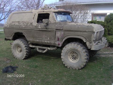 1978 Ford Bronco - This heavily muddied 1978 Ford Bronco sits on a grassy area, showing its off-road modifications and weathered condition.