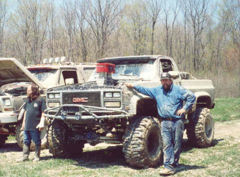 1978 Ford Bronco - A man poses with a heavily modified GMC pickup truck, its massive tires and exposed engine hinting at its off-road capabilities.