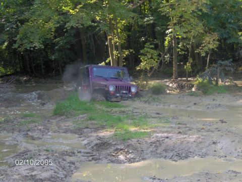 1978 Ford Bronco - A Jeep navigates a difficult muddy path, kicking up dirt as it goes.