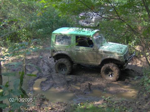 1978 Ford Bronco - A green off-road vehicle navigates a muddy trail, with another vehicle partially visible behind it.