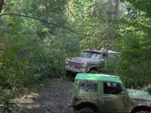 1978 Ford Bronco - Two off-road vehicles navigate a wooded trail on a sunny day.