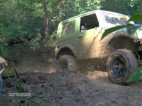 1978 Ford Bronco - This green off-road vehicle is deep in the mud, struggling to move forward.