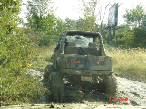 1978 Ford Bronco - This heavily modified off-road vehicle is navigating a muddy trail surrounded by vegetation.