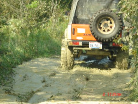 1978 Ford Bronco - An orange off-road vehicle navigates a muddy trail, kicking up dirt as it goes.