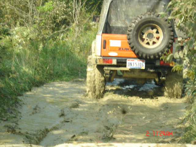 Orange off-road vehicle with spare tire on back, driving through mud