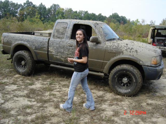 Mud-covered extended-cab pickup truck in a field with a woman walking past