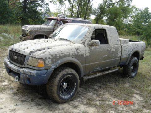 1978 Ford Bronco - A muddy pickup truck is parked in a field with another vehicle in the background.