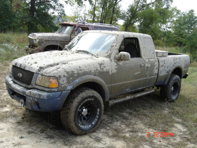 Mud-covered pickup truck, 3q-front view. Another vehicle is behind it