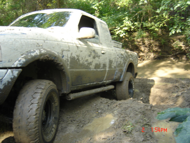 Mud-covered pickup truck navigating a muddy trail with trees in the background