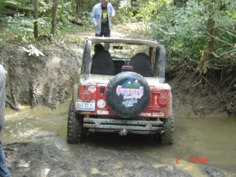 1978 Ford Bronco - Jeep Wrangler navigates a muddy trail with water obstacles.