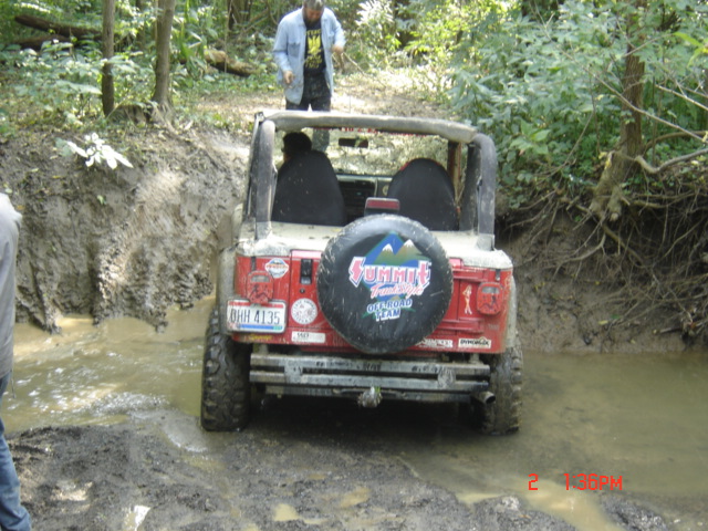 Red Jeep Wrangler with spare tire cover, driving through muddy water. License plate reads OHH 4135