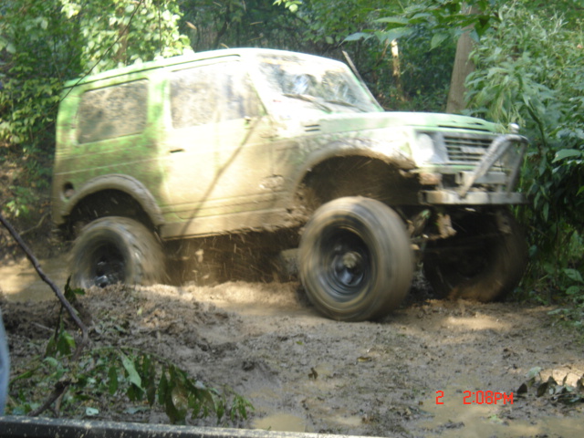 Green off-road vehicle with large tires driving through mud, front bumper visible