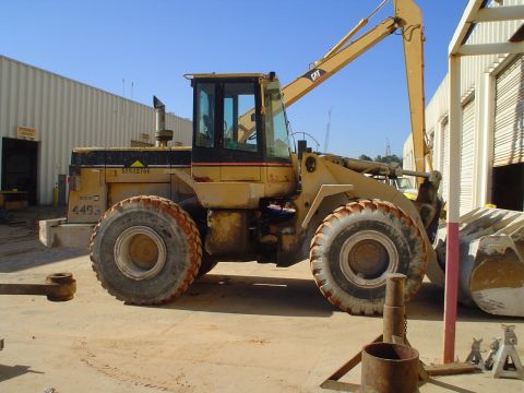 1966 International School Bus - A yellow Caterpillar wheel loader sits idle on a dirt lot next to a large industrial building.