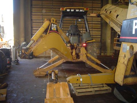 1966 International School Bus - A yellow backhoe loader with the CAT logo is parked indoors, with other heavy machinery visible in the background.