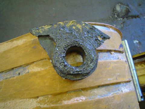 1966 International School Bus - Close-up of a heavily corroded metal part with a central hole, placed on a wooden structure.