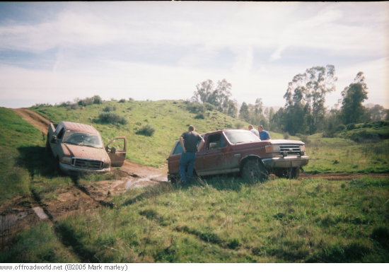 Two trucks stuck in a muddy ditch on a grassy hill