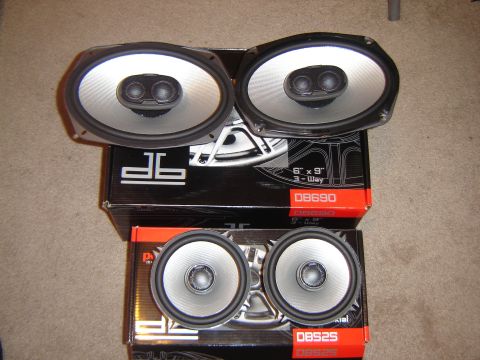 1988 Ford LTD Crown Victoria - Two pairs of car speakers, one set oval and one set round, are displayed on their packaging boxes.