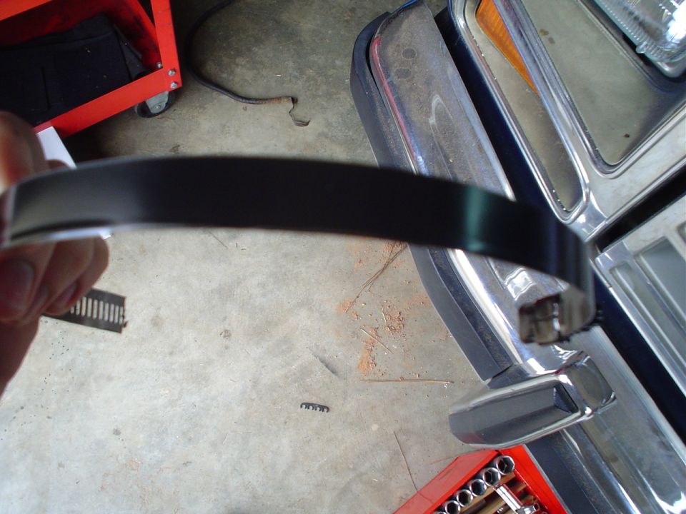 Hand holding black trim piece near 1984 Ford Bronco fender and grille
