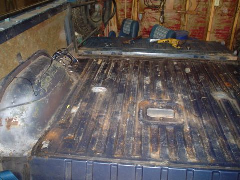 1984 Ford Bronco - The interior of a vehicle shows a worn floor and seats, with tools and a spare tire in the background.