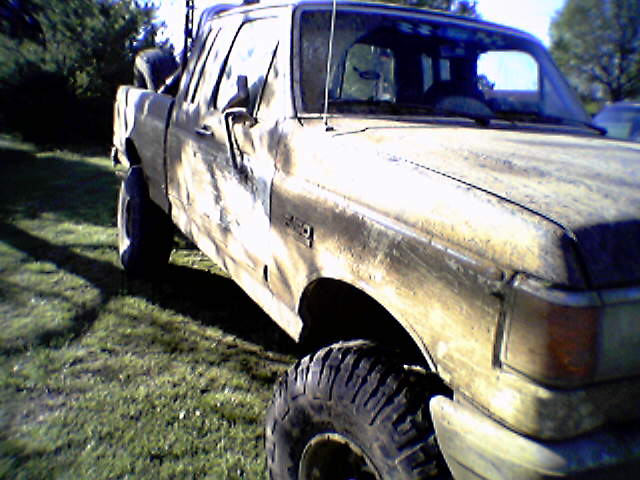 Mud-covered lifted Ford F-150 extended cab pickup with large off-road tires, side view on grass