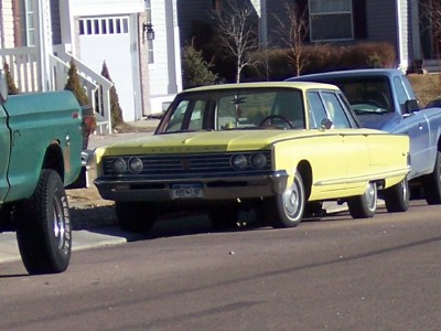 1972 Ford Ranchero - A yellow 1965 sedan is parked on the street next to two pickup trucks.