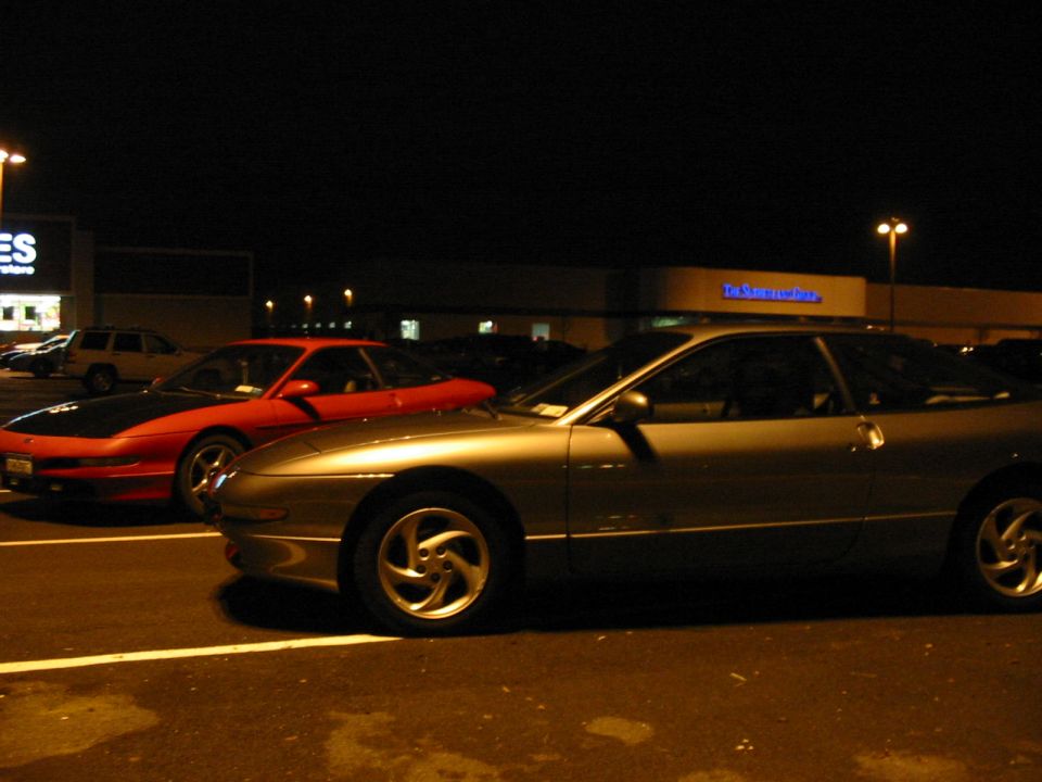 Two 1996 Ford Probes parked in a parking lot at night, one silver and one red with a black hood