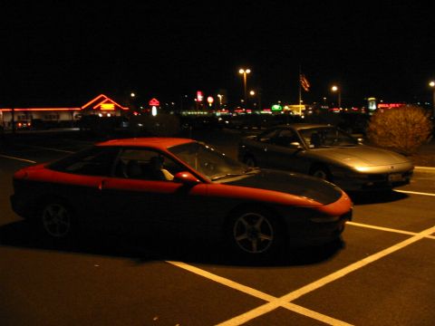 1996 Ford Probe - Two cars are parked in a lot at night, with commercial buildings visible in the background.