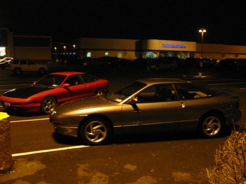 1996 Ford Probe - Two Ford Probe coupes are parked in a lot at night, illuminated by streetlights.