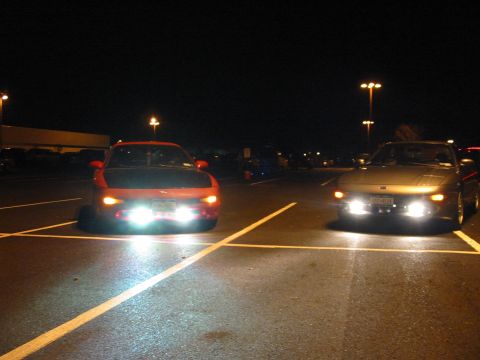1996 Ford Probe - Two cars are parked in a lot at night, their headlights illuminating the wet asphalt.