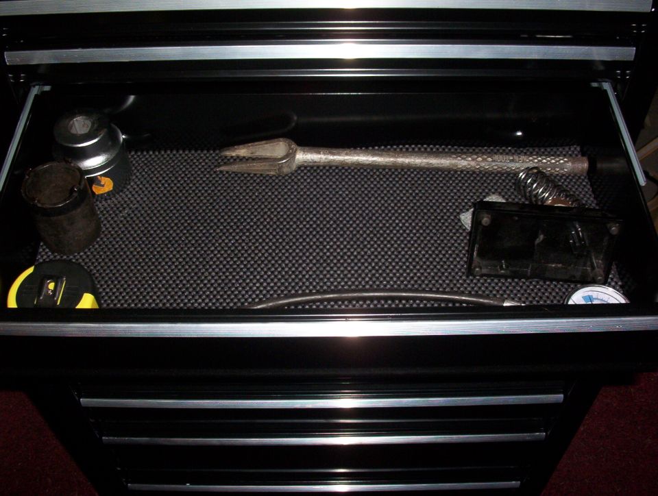 Open toolbox drawer with a tape measure, socket, pry bar, and other tools on a textured mat