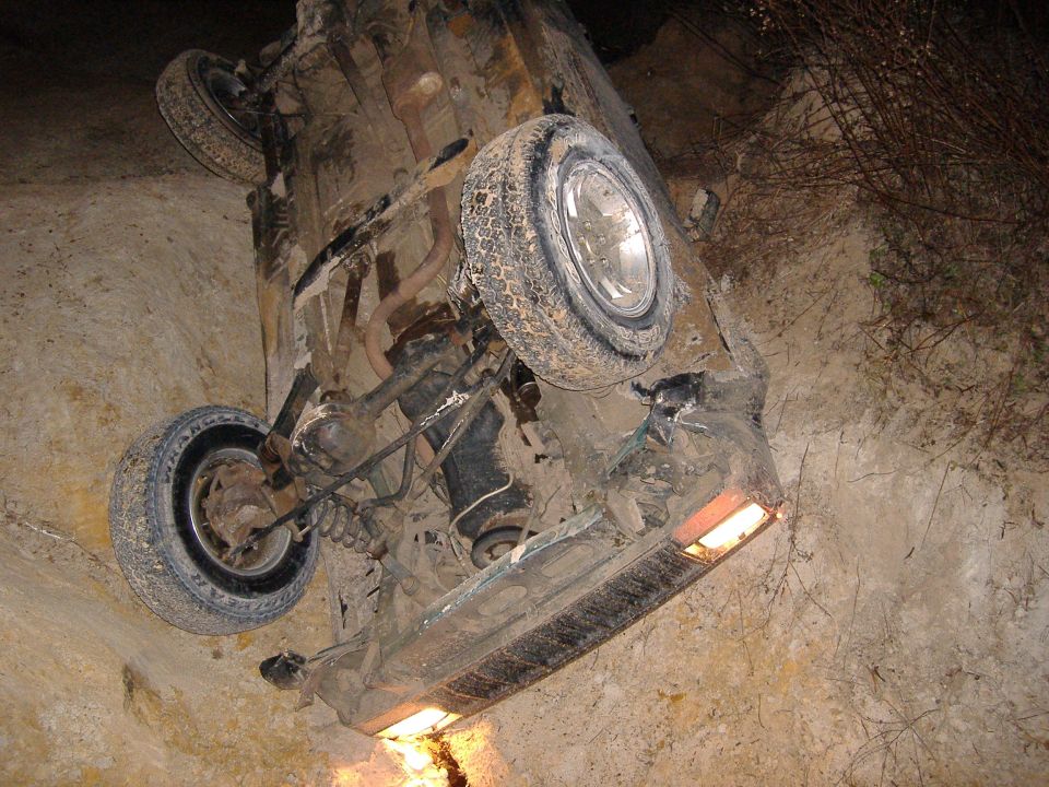Vehicle flipped on its side in a dirt ditch, showing undercarriage and wheels