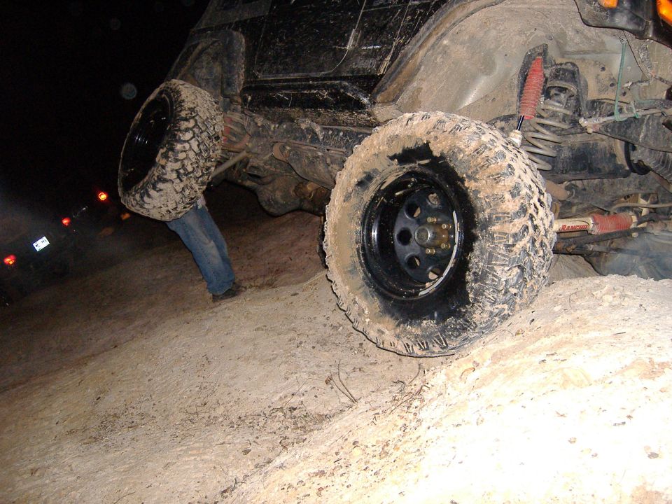 Black Jeep Wrangler tilted on its side, mud-covered tires, person in jeans visible